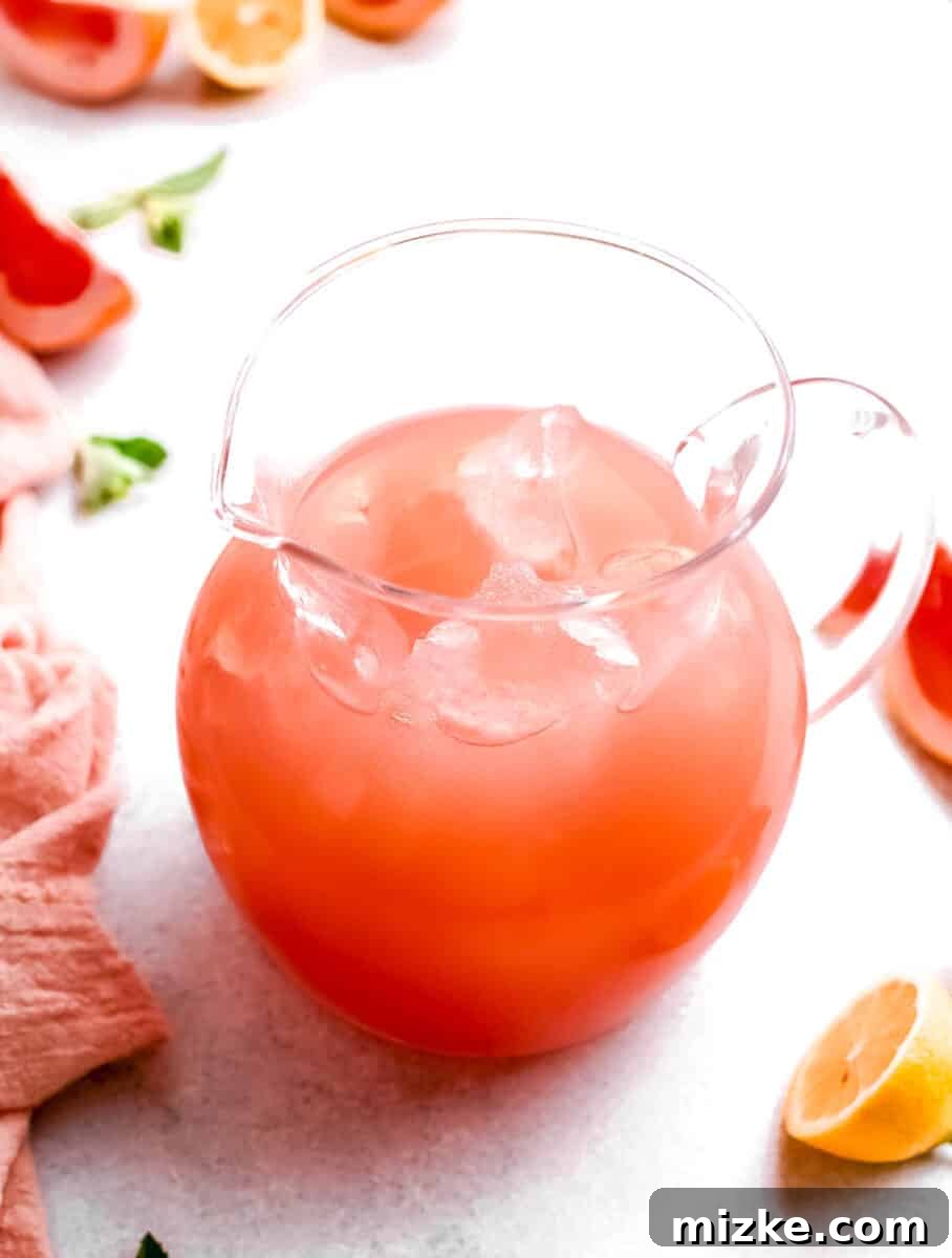 Paloma: A Deep Dive into the Iconic Cocktail 5 A large, transparent pitcher is filled to the brim with a pre-mixed Paloma cocktail, adorned with fresh lime and grapefruit slices, ready for serving a group of guests.