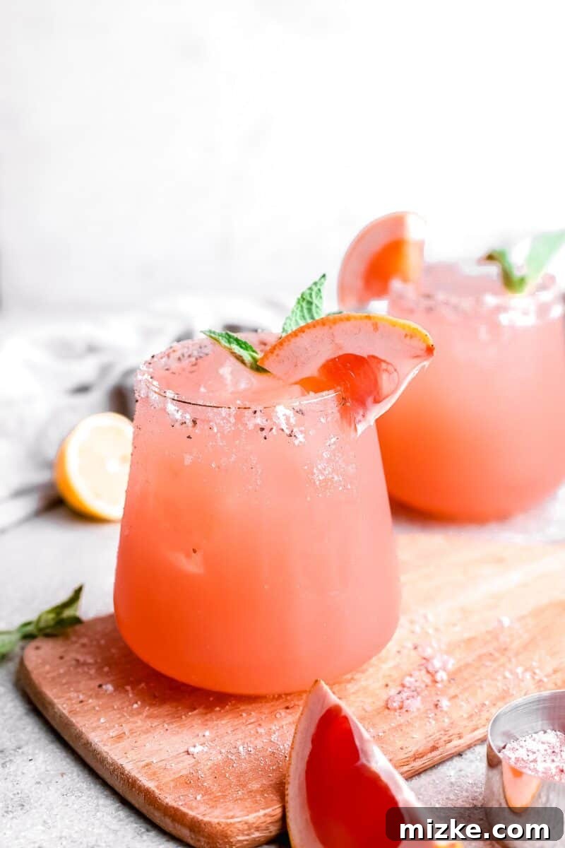 Paloma: A Deep Dive into the Iconic Cocktail 7 Two perfectly prepared Paloma cocktails, garnished with bright lime wedges, gracefully resting on a rustic wooden cutting board, ready for indulgence.