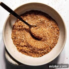 A bowl filled with bbq dry rub seasoning mix and a spoon, placed on a white surface.