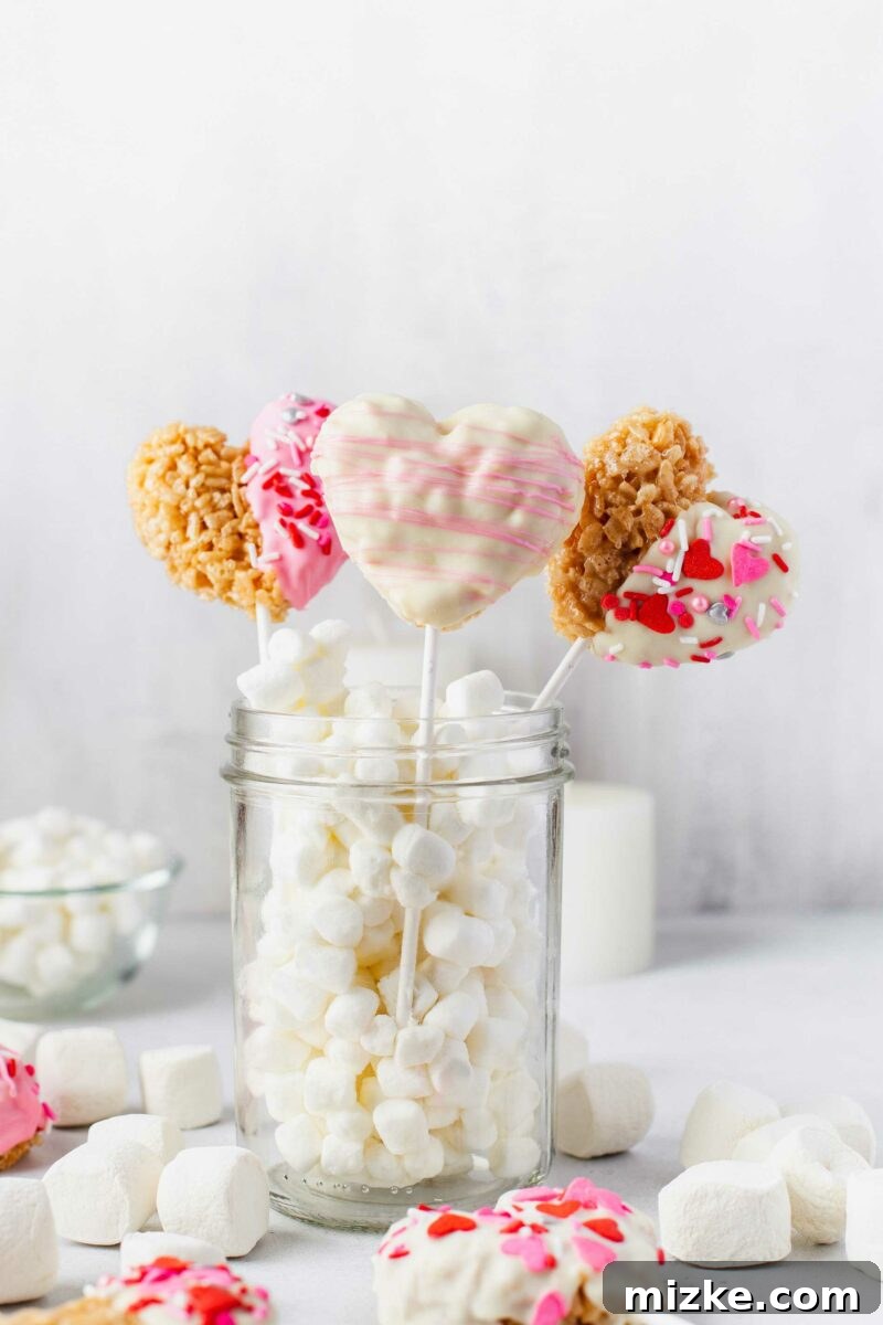 Sweetheart Krispy Delights 2 Three heart shaped rice krispie treats on white lollipop sticks are placed in a jar filled with mini marshmallows, ready for Valentine's Day gifting.