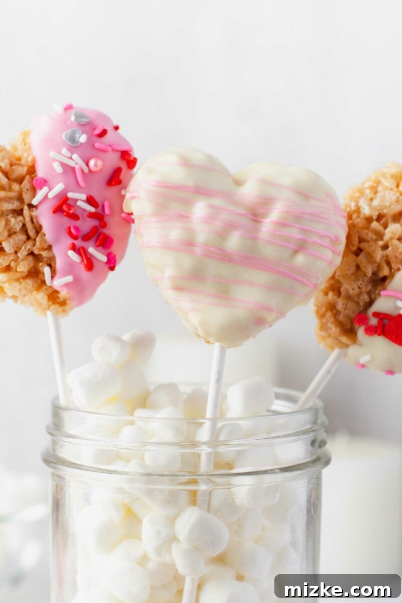 Sweetheart Krispy Delights 3 Three perfectly formed heart-shaped Rice Krispie Treats are elegantly arranged in a glass jar, nestled amongst a bed of fluffy mini marshmallows, creating an inviting display.