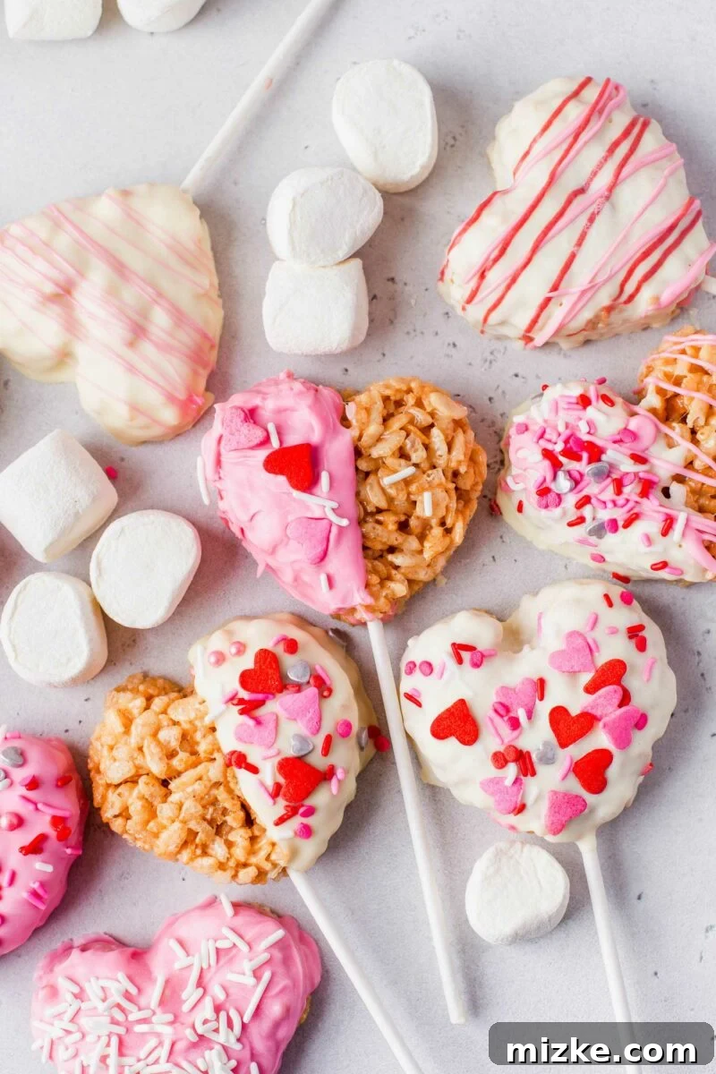 Sweetheart Krispy Delights 6 Multiple heart-shaped Rice Krispies treats are arranged on white lollipop sticks, placed alongside mini marshmallows on a chic gray surface, highlighting their readiness for a sweet celebration.