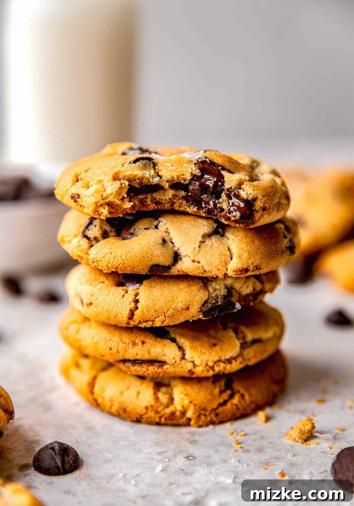 A stack of golden-brown chocolate chip cookies with gooey, melted chocolate visible. The top cookie has a bite taken out of it, revealing its soft interior.