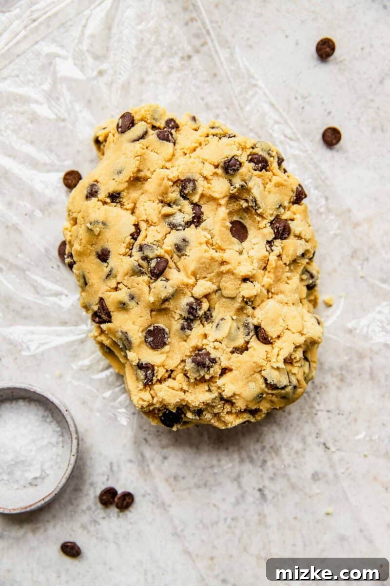 Placing freshly prepared chocolate chip cookie dough onto a sheet of plastic wrap on a counter.
