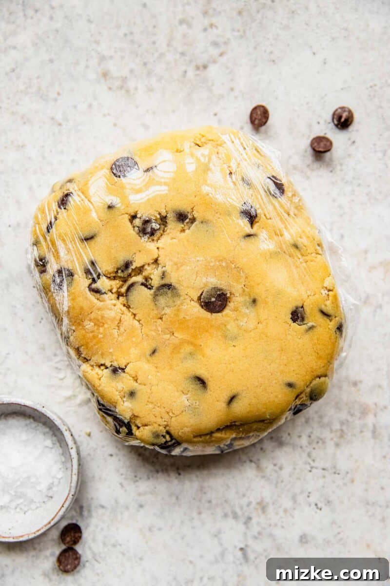 Chocolate chip cookie dough tightly wrapped in plastic wrap, ready for chilling in the refrigerator.