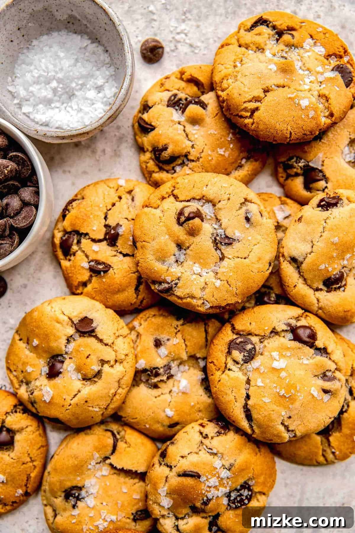 An overhead image of a large, tempting pile of golden chocolate chip cookies, dusted with sea salt.
