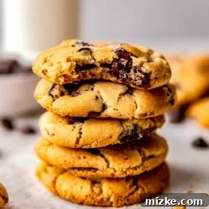 A stack of perfectly baked chocolate chip cookies. The top cookie has a bite taken out of it, revealing a soft, chewy interior with melted chocolate.