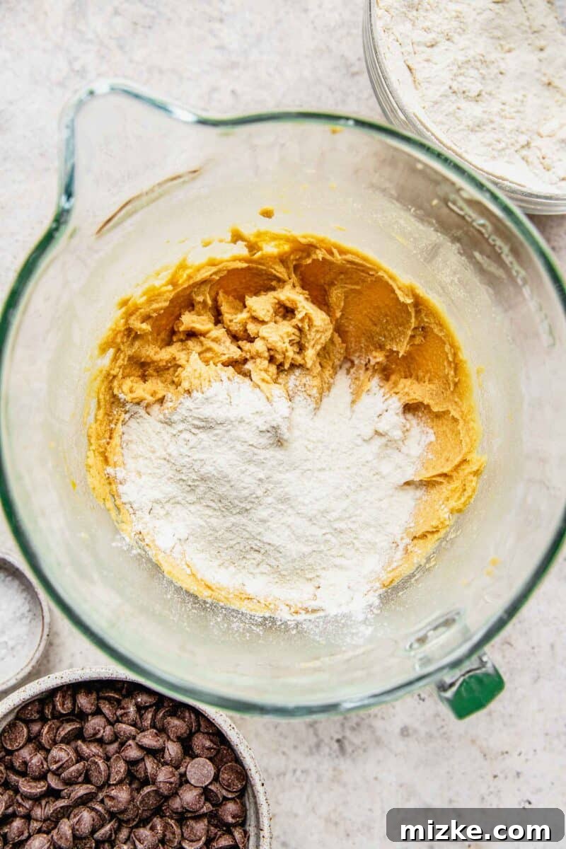 Slowly adding the sifted dry ingredients into the wet butter and sugar mixture in a stand mixer.