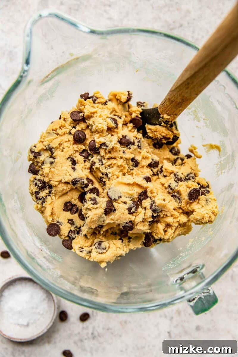 Folding dark chocolate chips into the prepared cookie dough with a spatula.