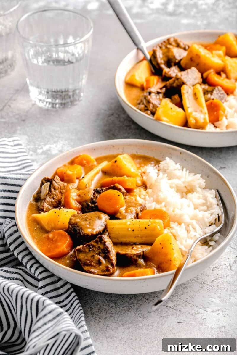 Golden Japanese Curry 4 beef, potatoes, celery, and carrots in a stew-like sauce on a bed of white rice in a rimmed ceramic bowl with a fork next to it. a striped linen towel and a glass of water can be seen
