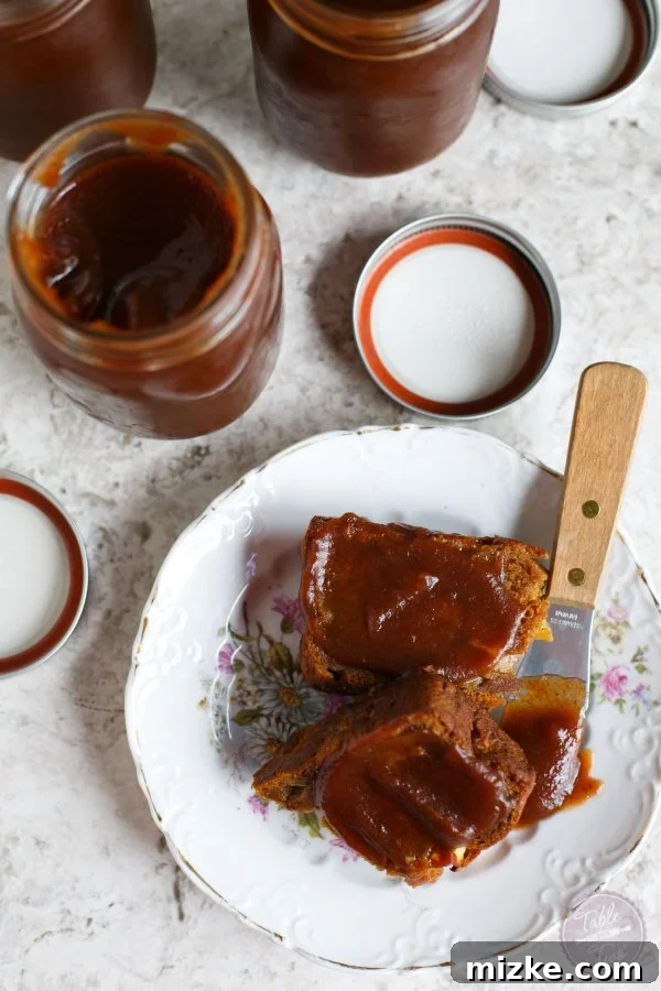 Spiced Slow Cooker Bourbon Apple Butter 2 A jar of rich, amber Slow Cooker Bourbon Apple Butter, garnished with cinnamon sticks and fresh apples, evoking cozy fall vibes.
