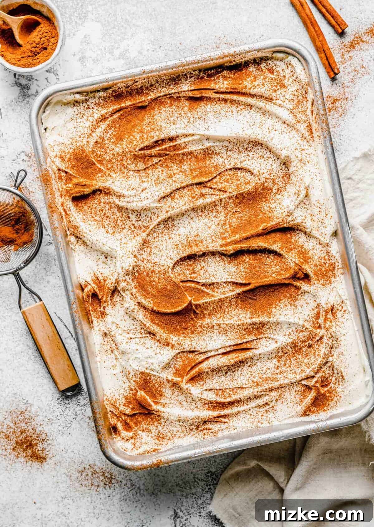Tres Leches Cake beautifully garnished with cinnamon and ready to serve. Prepared Tres Leches Cake in a pan, with a bowl of cinnamon and cinnamon sticks nearby.