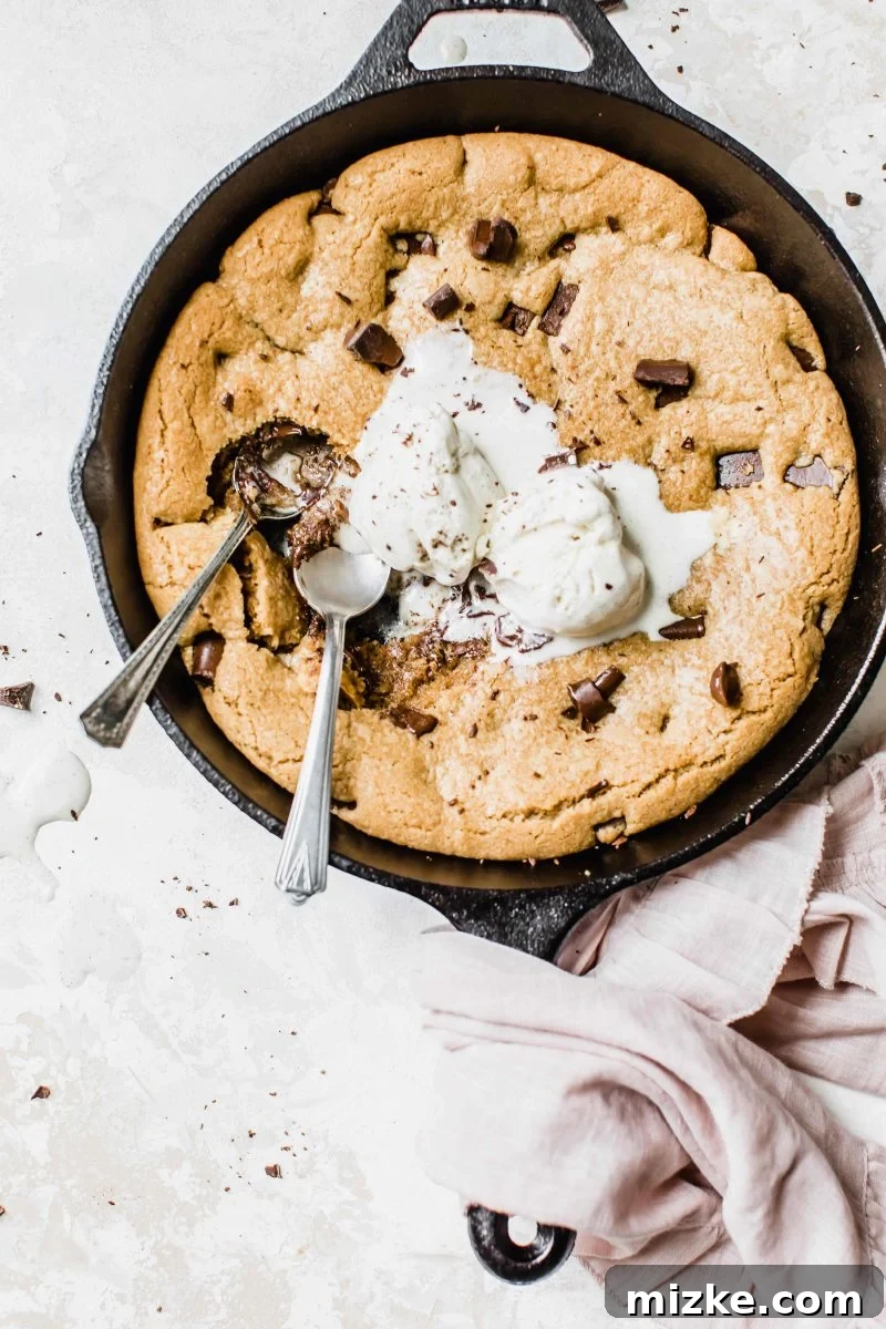 A perfectly baked coconut chocolate chunk skillet cookie with a scoop removed, revealing a soft, gooey interior and melted chocolate. The edges are golden and slightly crisp.