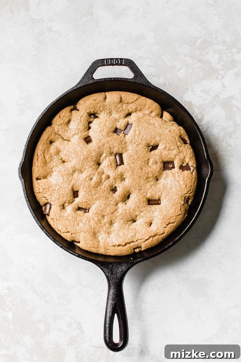 Close-up shot of the skillet cookie, showcasing its beautiful golden-brown crust and generous dark chocolate chunks peeking through the dough. The texture promises both crispiness and chewiness.