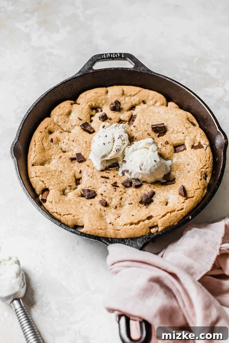 A warm skillet cookie, freshly baked and glistening with melted chocolate, ready to be served. The rich brown color suggests a deeply satisfying flavor profile.
