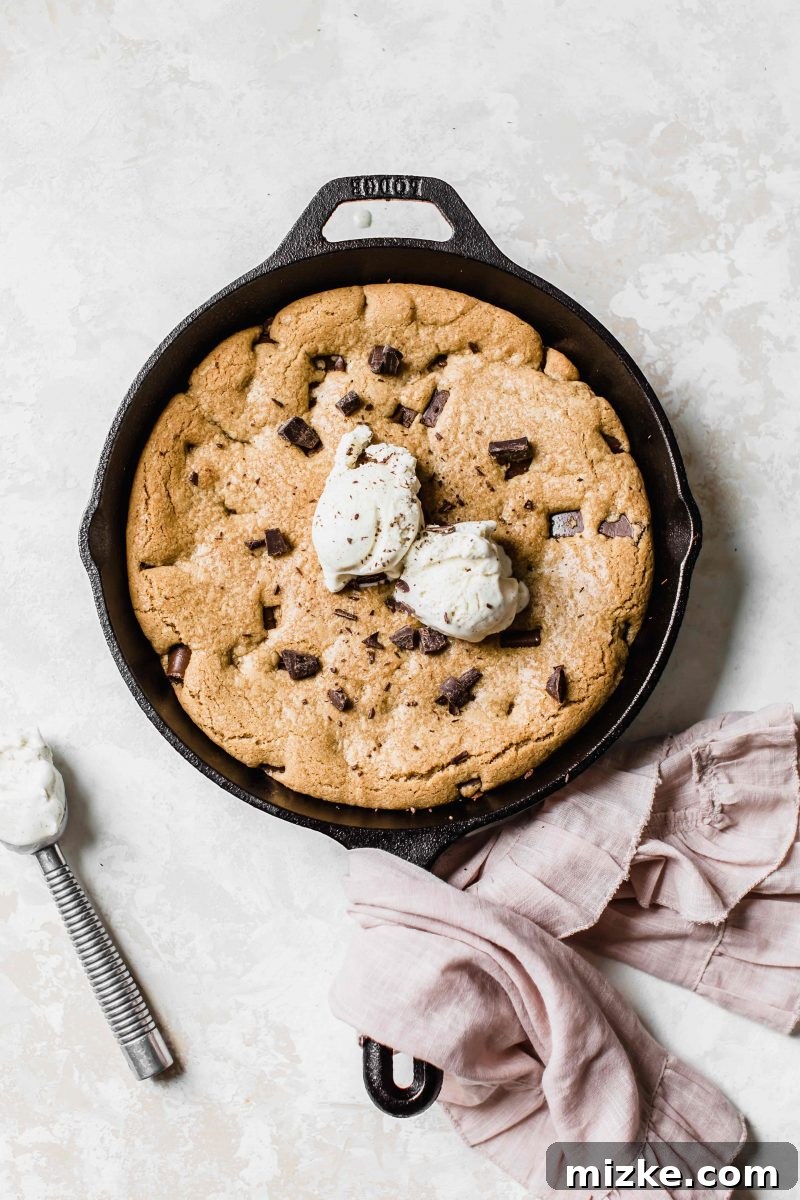 An overhead shot of the skillet cookie, adorned with scoops of vanilla ice cream, creating a delightful contrast between the warm cookie and cold cream. Drizzled with chocolate sauce, it looks like an ultimate dessert.