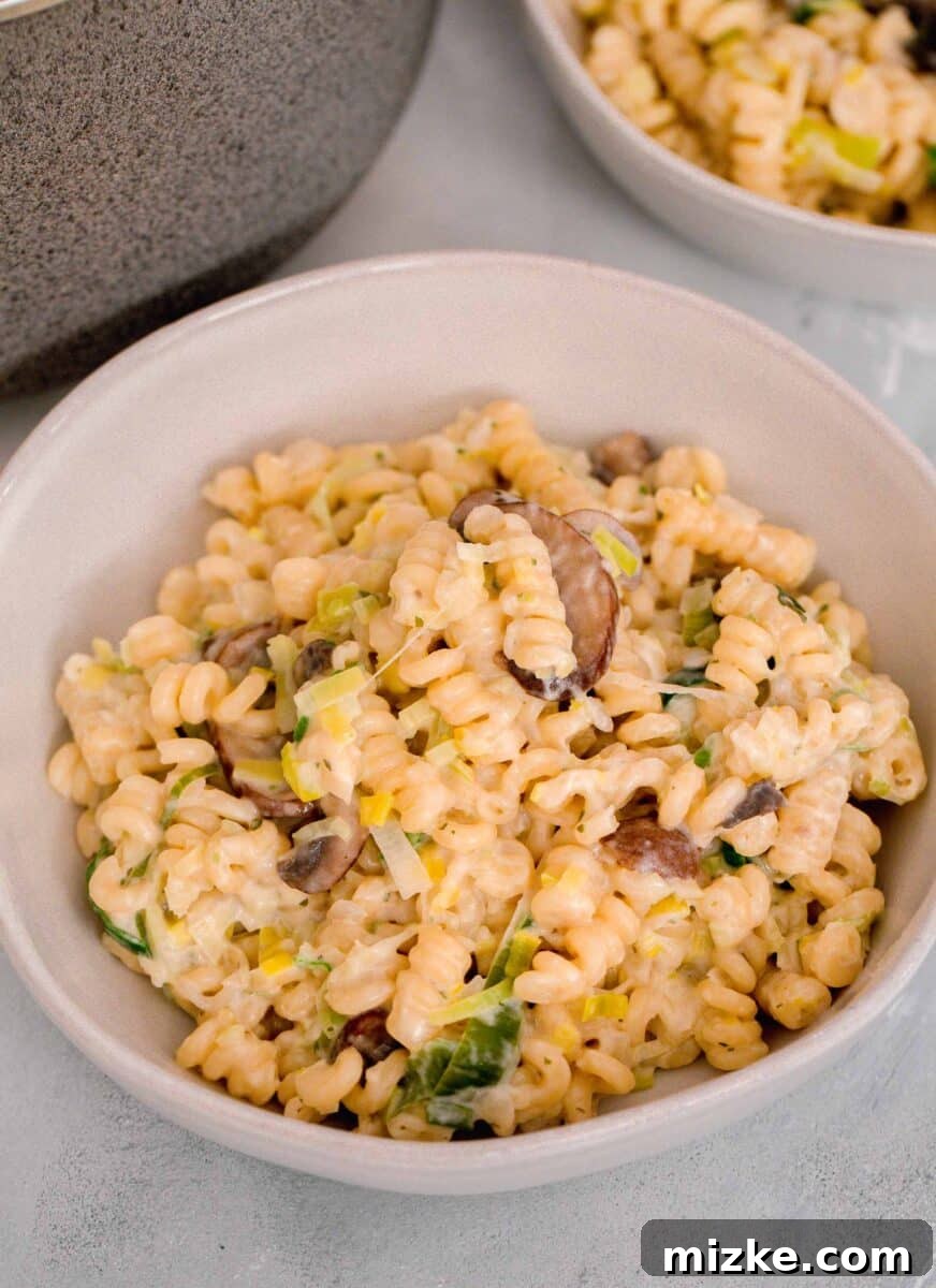 Velvety Mushroom and Leek One-Pot Pasta 12 Creamy mushroom and leek pasta served in an elegant beige ceramic bowl, with another bowl of pasta in the background.
