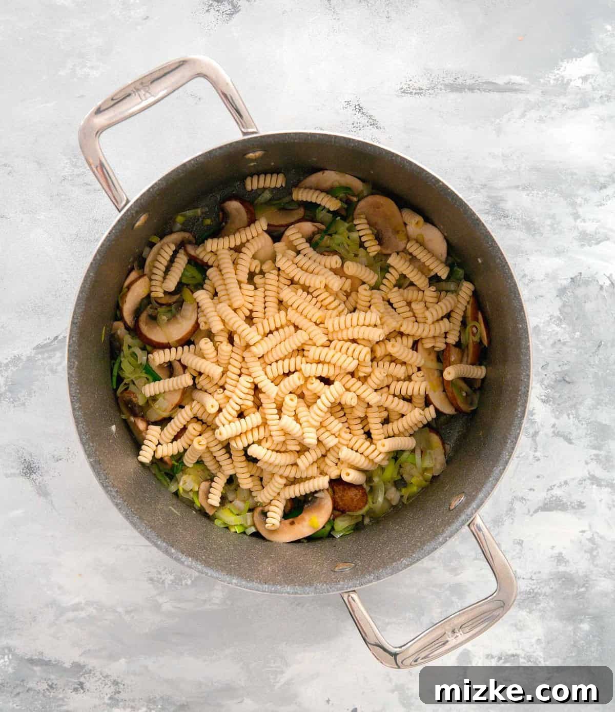Velvety Mushroom and Leek One-Pot Pasta 8 Uncooked spiral pasta being added to the pot with the cooked leeks, onions, garlic, and mushrooms.