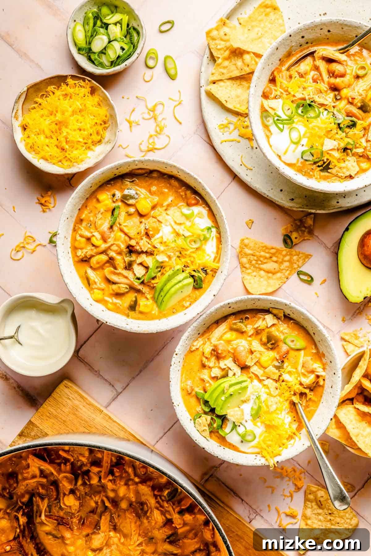 Smoky Southwest Chicken Chili 2 Southwest Chicken Chili is portioned out into several bowls, garnished generously with crushed tortilla chips, shredded cheese, and fresh avocado slices on top.