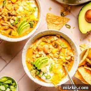 Two bowls of Southwest Chicken Chili topped with shredded cheese, avocado slices, sour cream, and tortilla chips