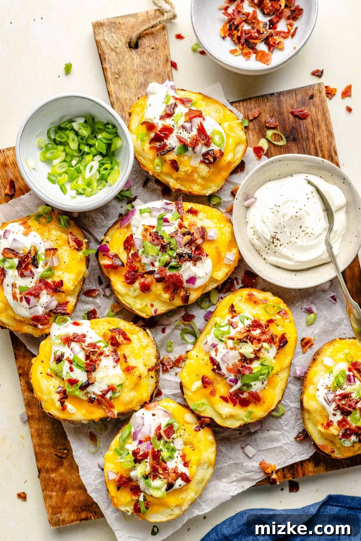 Loaded Double-Baked Potatoes 2 Delicious twice baked potatoes topped with crispy bacon, fresh green onions, and a side of sour cream, ready to serve as a perfect party appetizer.