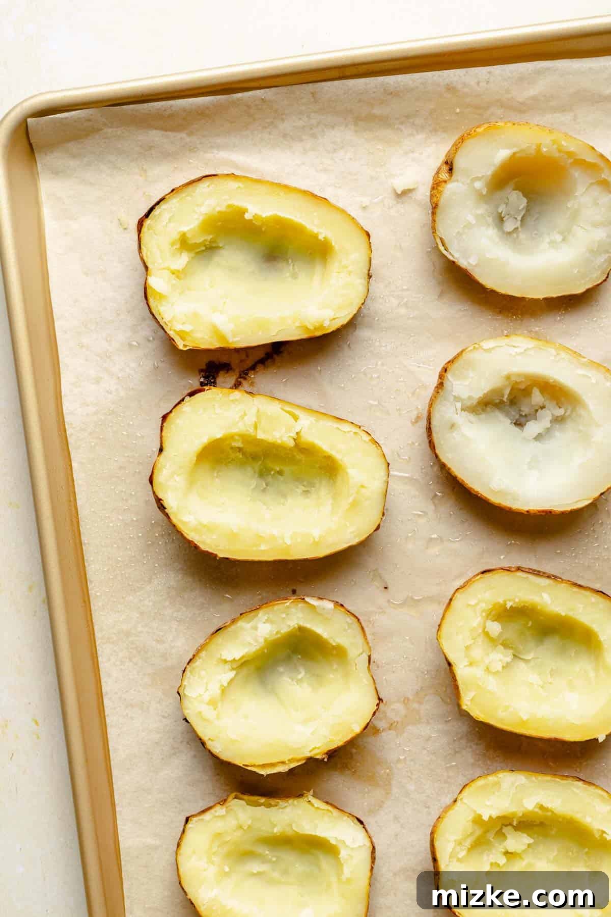 Loaded Double-Baked Potatoes 3 Baked potatoes with their fluffy insides scooped out and placed into a bowl, leaving a perfect potato skin shell on a baking sheet.