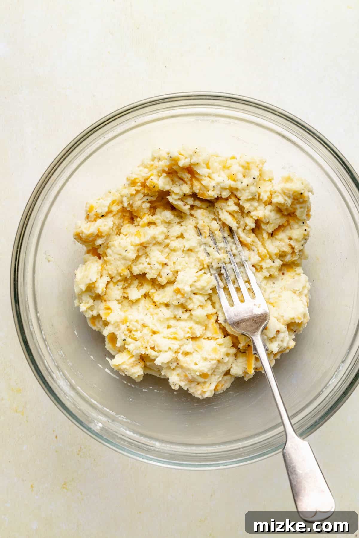 Loaded Double-Baked Potatoes 4 A fork mashing a creamy mixture of potato filling, cheese, and other ingredients in a glass bowl, creating the delicious filling for twice baked potatoes.