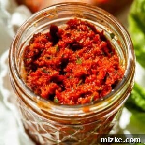 A close-up of vibrant sun-dried tomato pesto stored in a clear glass mason jar, ready for use in culinary creations.