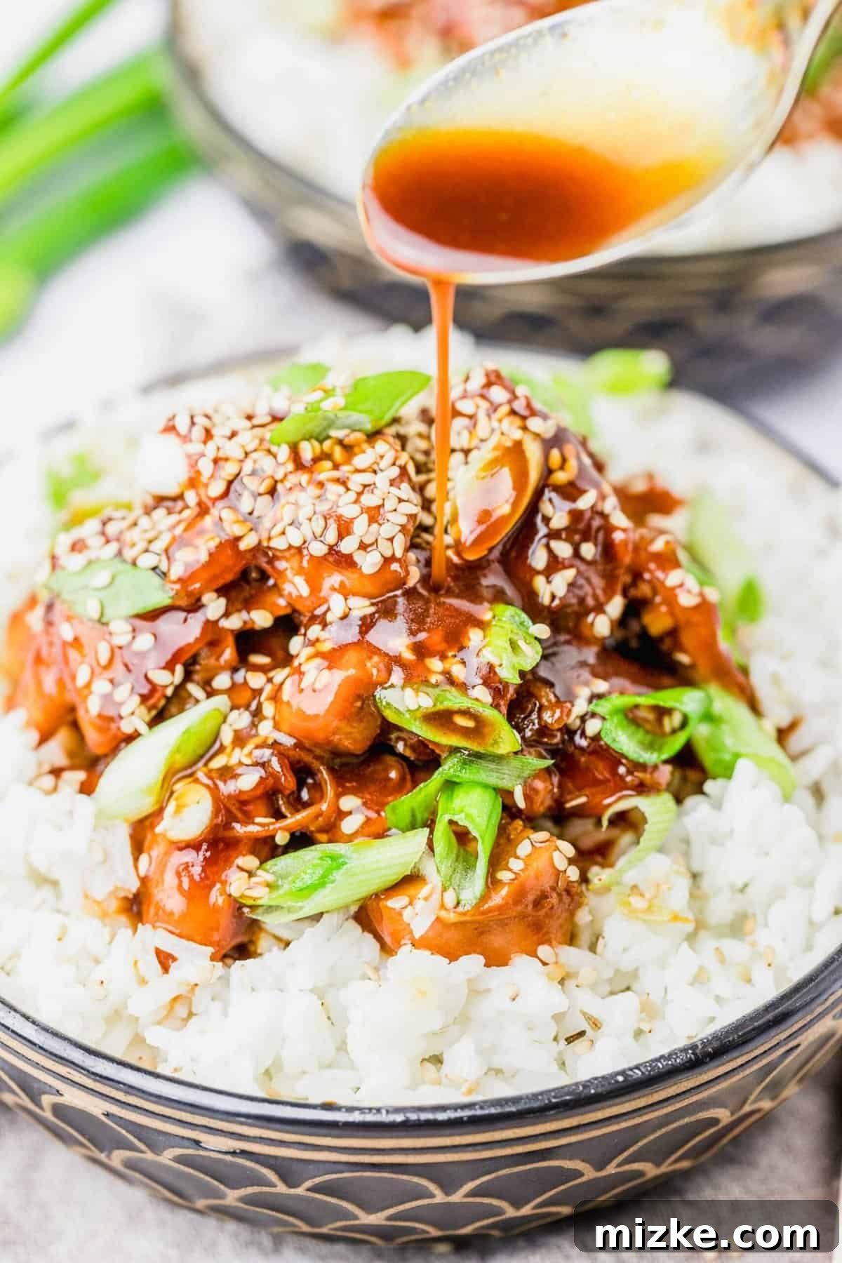 Sauce Drizzling Over Honey Sesame Chicken and Rice A spoon elegantly drizzles the rich, glossy honey sesame sauce over a bowl of white rice topped with succulent chicken.