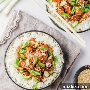 Two bowls of crockpot honey sesame chicken served over white rice, garnished with green onions