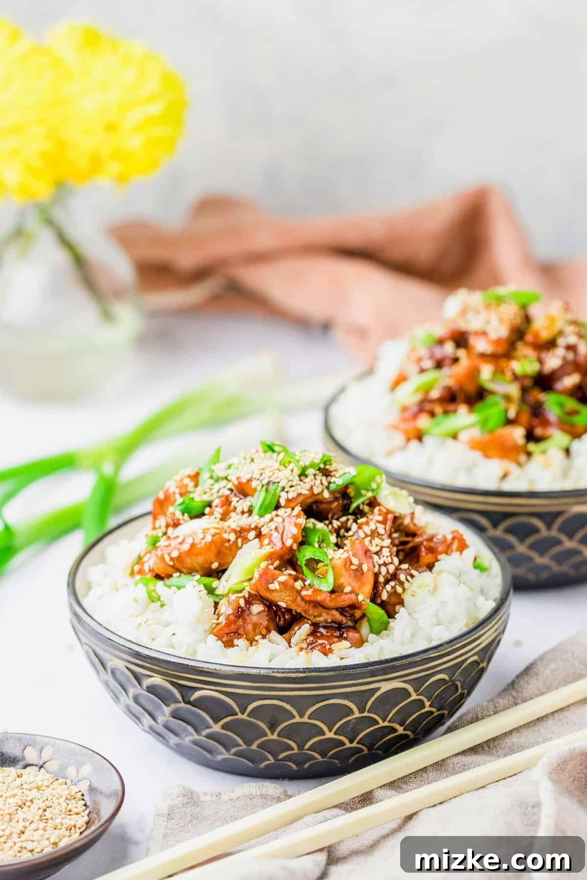 Delicious Honey Sesame Chicken Served with Rice and Green Onions Two enticing bowls brimming with fluffy white rice, generously topped with glistening honey sesame chicken and garnished with vibrant green onions.