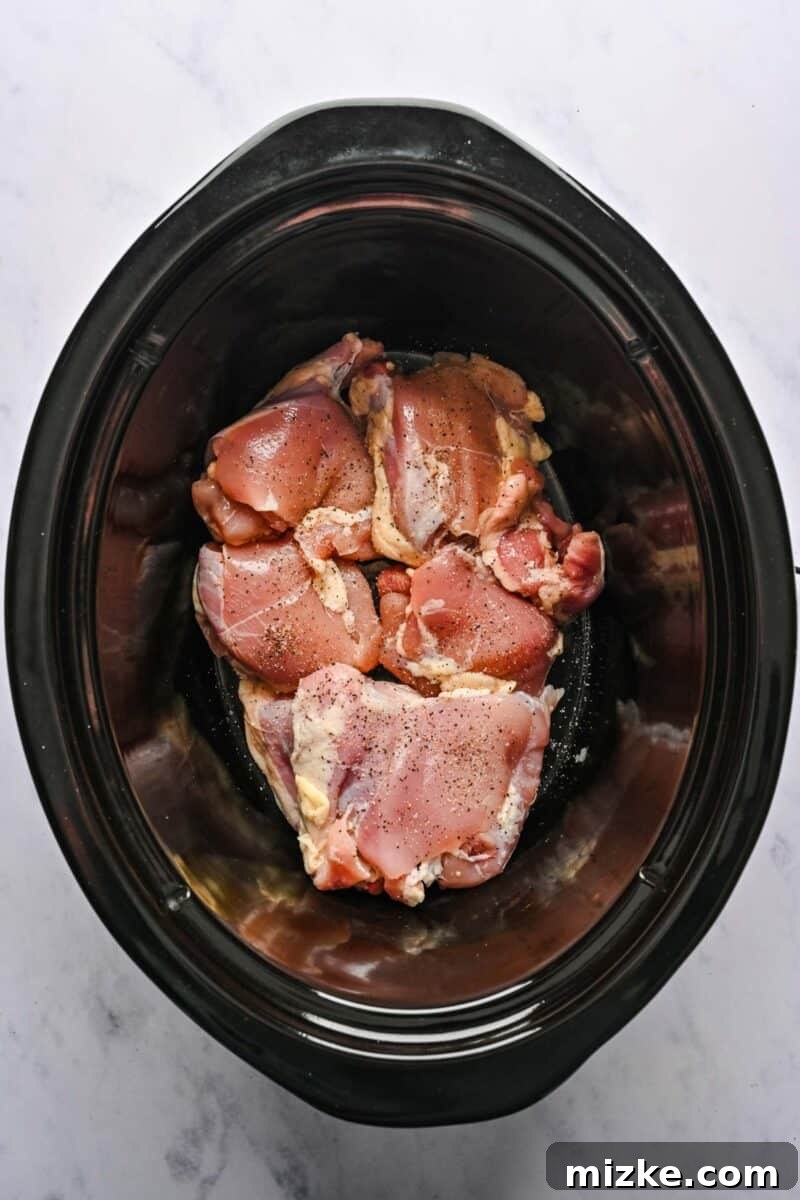 Preparing Chicken Thighs in the Crockpot Uncooked chicken pieces are carefully arranged at the bottom of a crockpot liner, ready for seasoning.