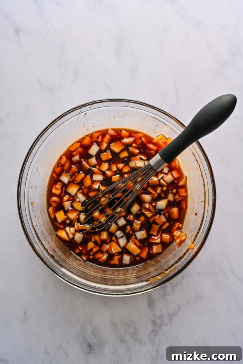 Whisking Together the Honey Sesame Sauce The savory-sweet sauce for honey sesame chicken is perfectly whisked together in a clear glass bowl, showcasing its rich texture and color.