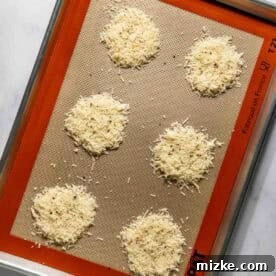 Six mounds of grated parmesan cheese on a silpat-lined baking sheet.