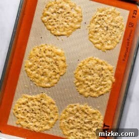 Six baked parmesan cheese crisps on a baking sheet lined with a silicone mat.