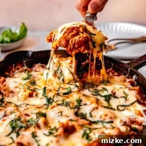 Scooping a serving of skillet lasagna out of the pan, emphasizing the rich sauce and cheese.
