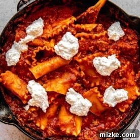 Adding dollops of ricotta and parmesan to skillet lasagna.