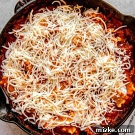 Adding shredded cheese to skillet lasagna.