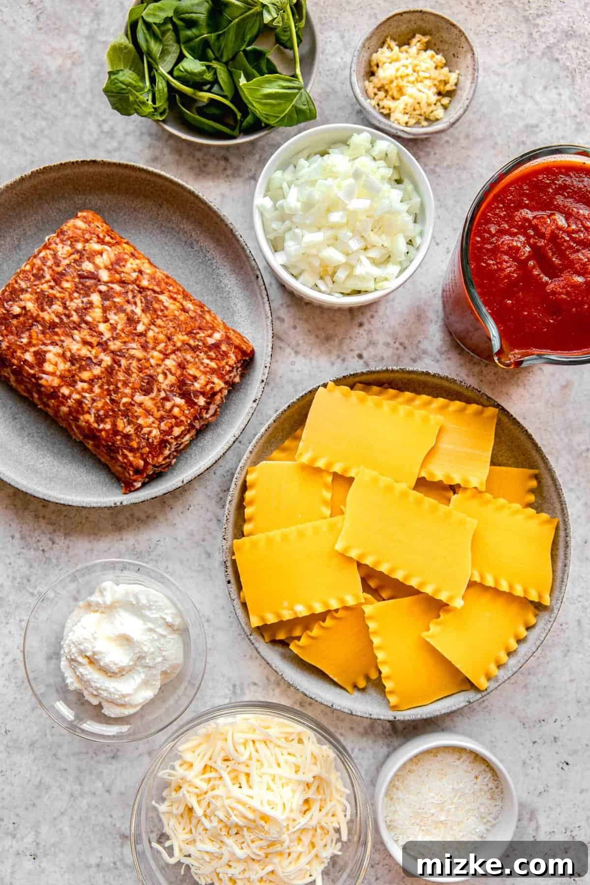 Assorted ingredients for skillet lasagna laid out on a kitchen surface, including sausage, marinara, cheese, and fresh basil.