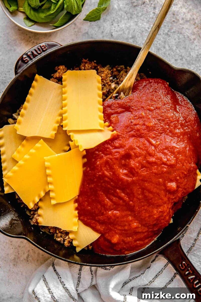 Stirring broken lasagna noodles and marinara sauce into the skillet with sausage, onions, and garlic.