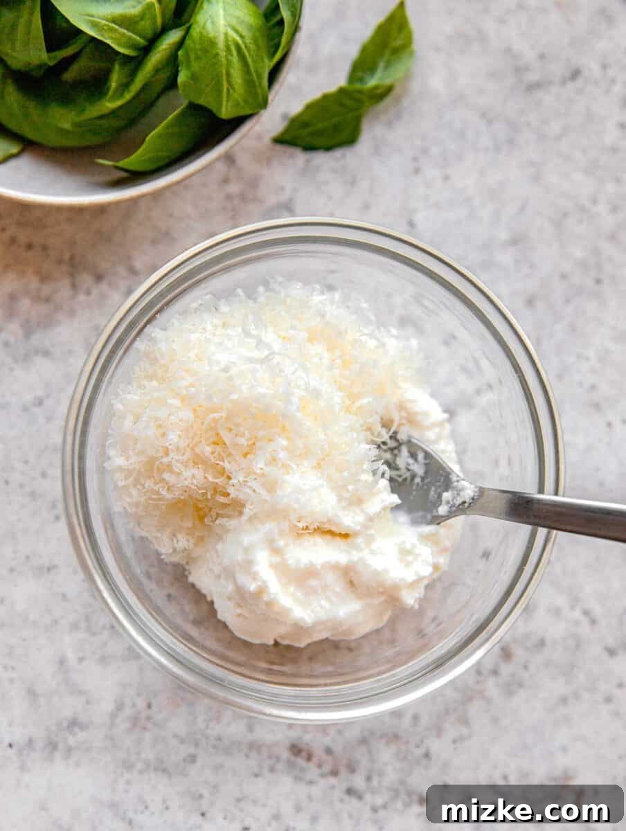 Adding ricotta and grated parmesan cheese to a mixing bowl.