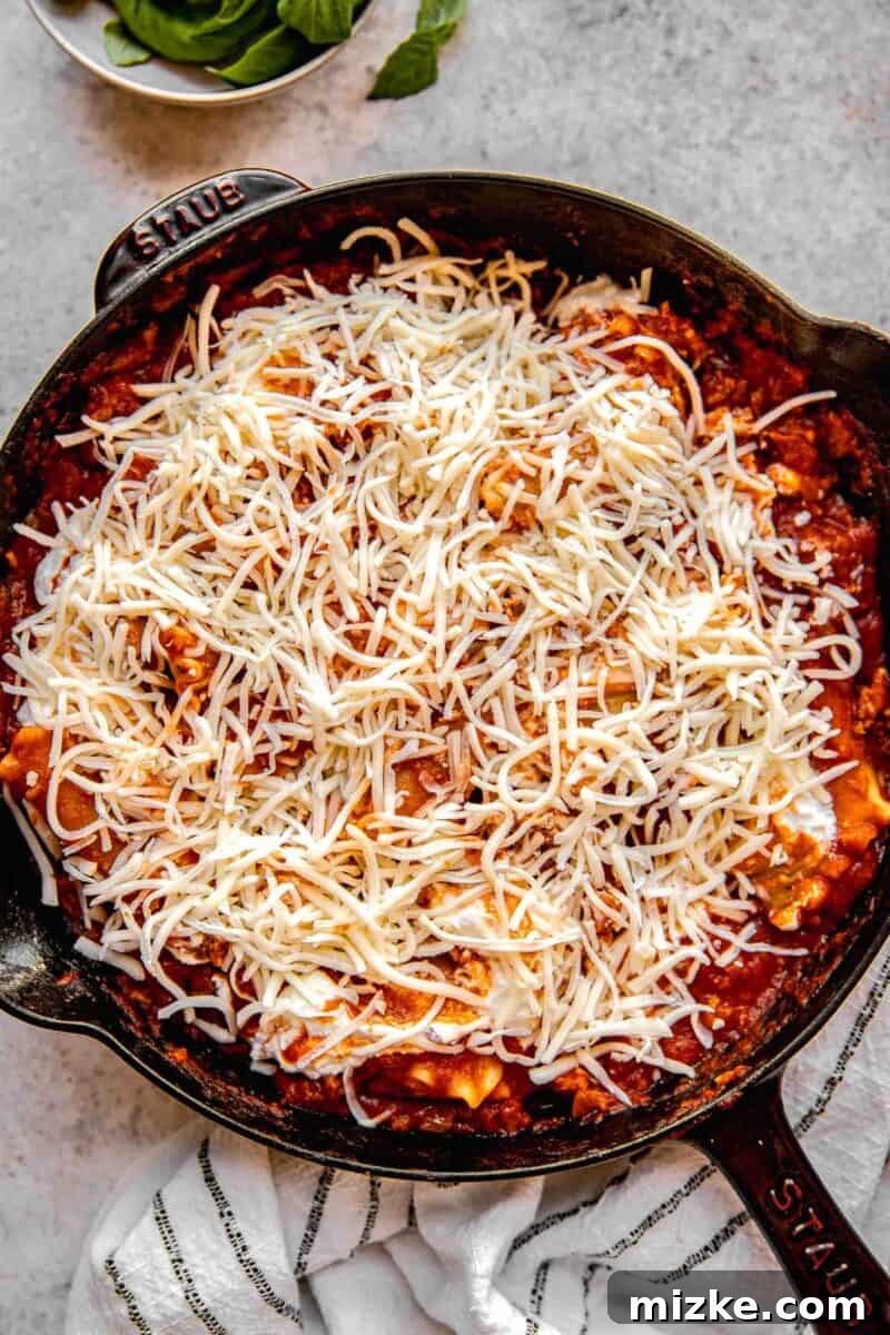 Sprinkling shredded mozzarella cheese over the skillet lasagna before broiling.