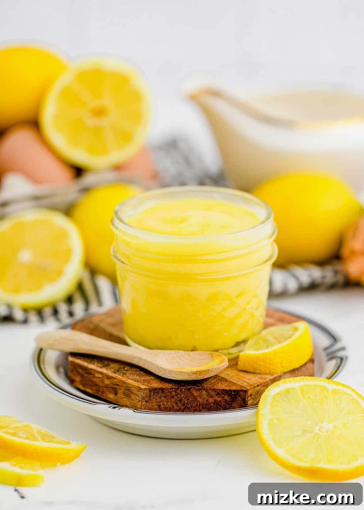 This homemade lemon curd recipe is thick, creamy, and buttery. It's so easy to make and perfect for topping toast, muffins, cakes, and more! Jar of vibrant homemade lemon curd with a spoon, surrounded by fresh, bright yellow lemons