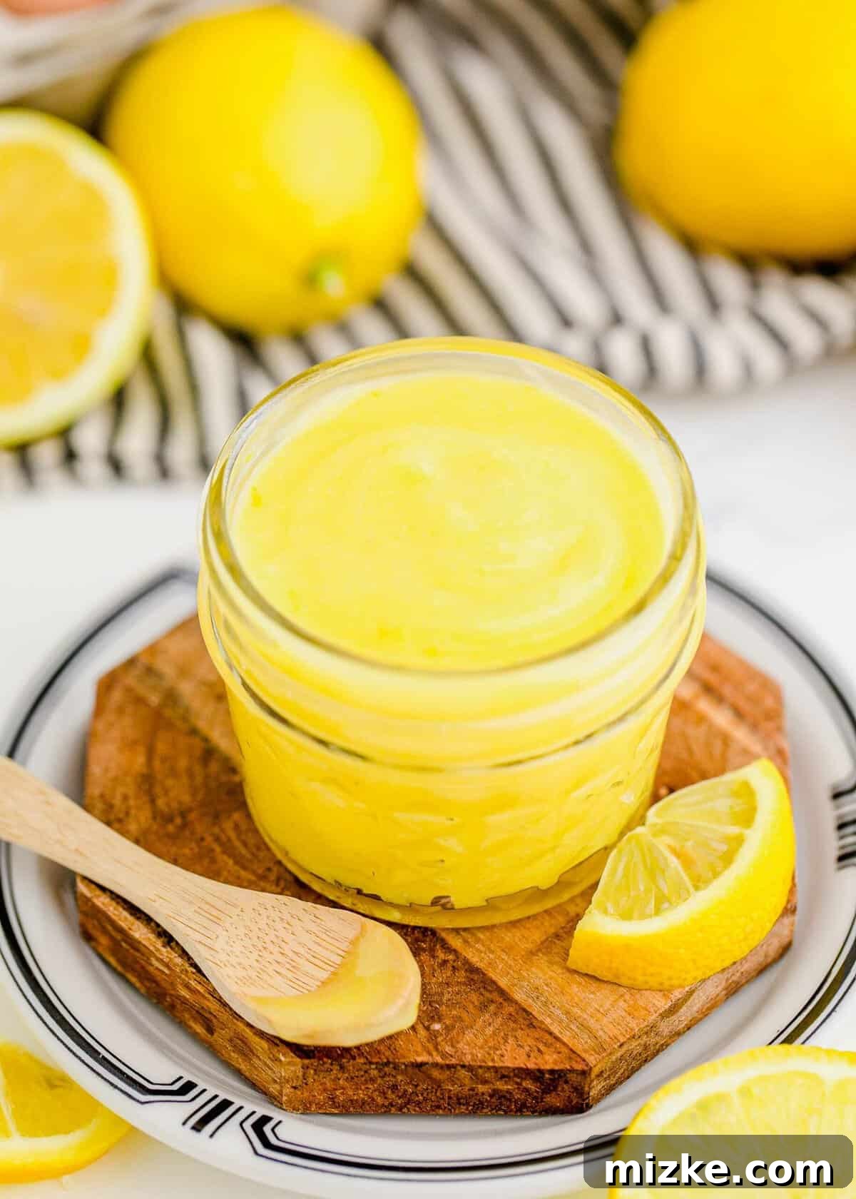 This homemade lemon curd recipe is thick, creamy, and buttery. It's so easy to make and perfect for topping toast, muffins, cakes, and more! Close-up photo of a jar of silky homemade lemon curd next to a spoon holding a perfect dollop of curd