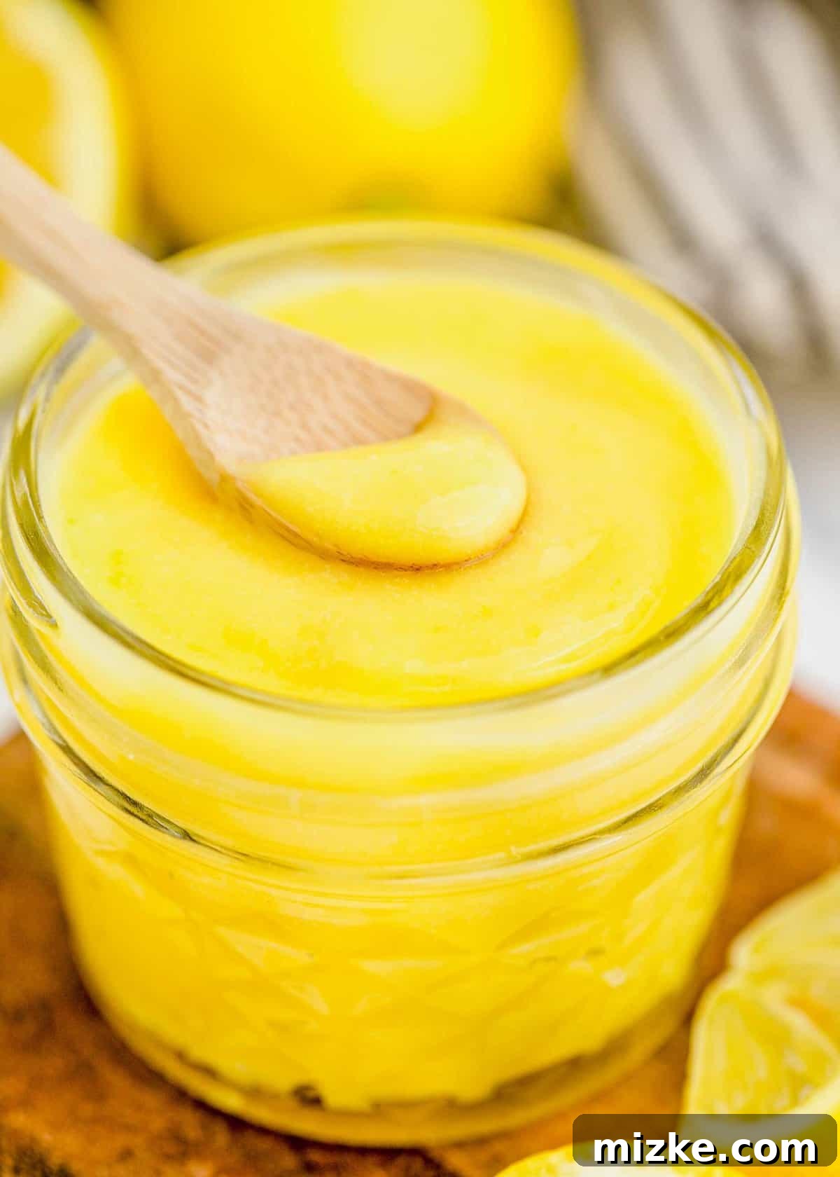 This homemade lemon curd recipe is thick, creamy, and buttery. It's so easy to make and perfect for topping toast, muffins, cakes, and more! A spoonful of perfectly smooth homemade lemon curd resting on the rim of a full glass jar