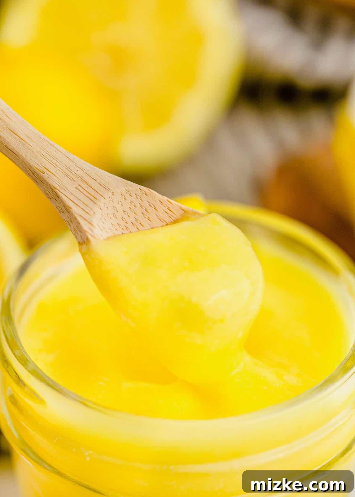 This homemade lemon curd recipe is thick, creamy, and buttery. It's so easy to make and perfect for topping toast, muffins, cakes, and more! A spoonful of homemade lemon curd being lifted from a glass jar, showcasing its smooth and creamy texture