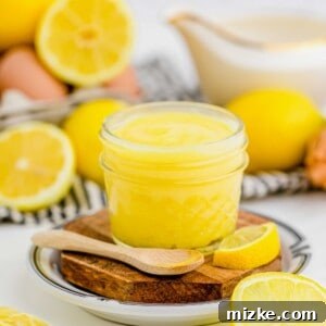 A spoonful of rich, creamy homemade lemon curd next to a jar with fresh lemons in the background, ready to be enjoyed. Jar of vibrant homemade lemon curd with a spoon in the foreground and fresh lemons in the background