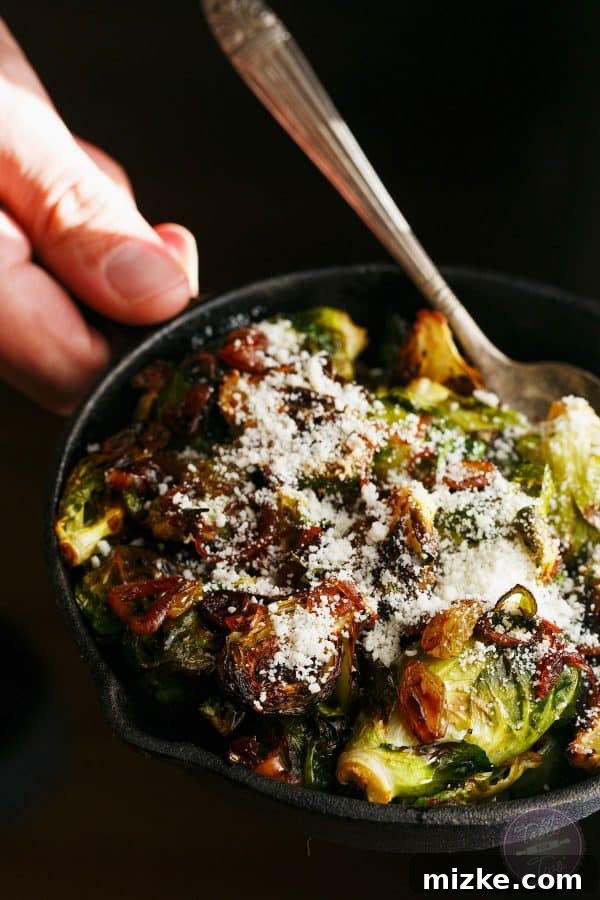 Close-up shot of the roasted brussels sprouts dish, showing the glossy caramelized shallots, sweet golden raisins, and savory cotija cheese crumbles.