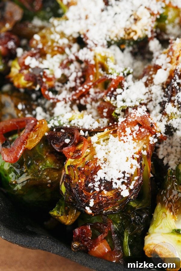A close-up of the roasted brussels sprouts in a bowl, ready to be served, showing the glistening balsamic glaze and cheese crumbles.