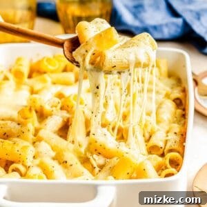 A wooden spoon lifts a scoop of creamy three cheese mac and cheese from the baking dish, showing the delicious texture.
